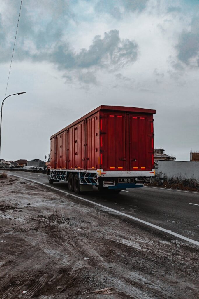 About Large heavy motor vehicle driving on roadway while transporting goods along village in cloudy day